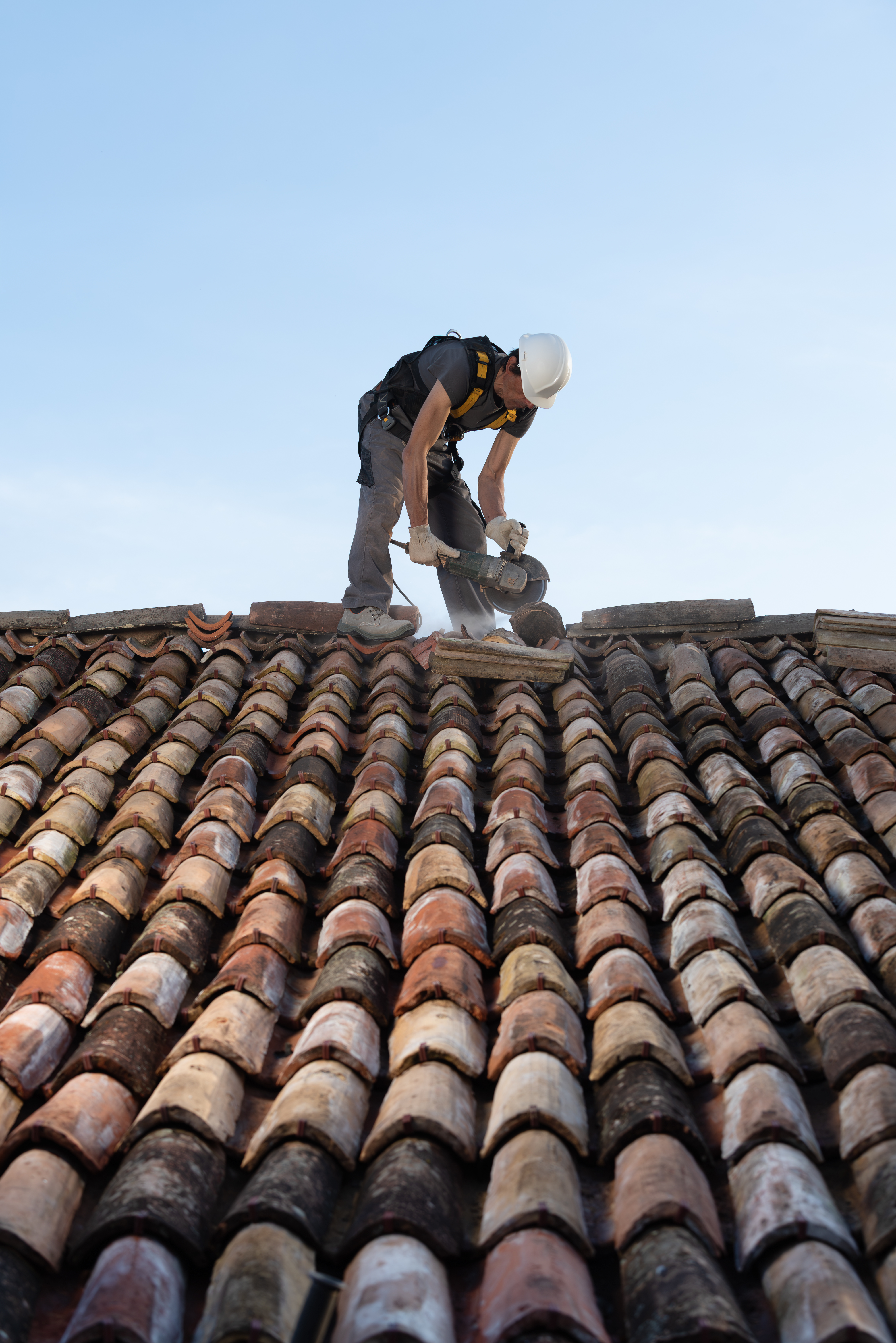 Professional roofer working on a residential clay tile roof, secured with a safety harness. Concept of home maintenance, construction safety, roofing work, and professional installation.